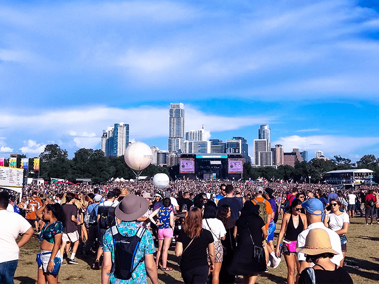 A crowd of people are walking in a field at a music festival reached using a limo party bus service.