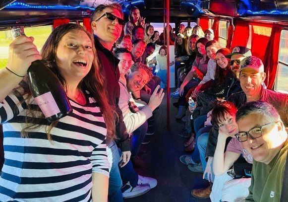 A group of people are standing on a bus holding bottles of champagne.